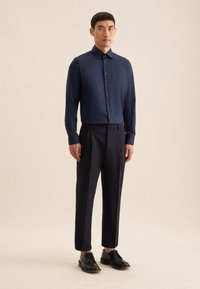 Marineblauw button-up shirt met een kraag, gecombineerd met donkere, strak gesneden broek en zwarte nette schoenen. Glad stof met lange mouwen en een aangesloten ontwerp.