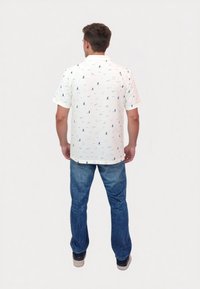 Kortærmet polo skjorte i hvid med blå sejlbåd og geometriske mønstre. Lavet af tekstureret stof; parret med blå jeans.