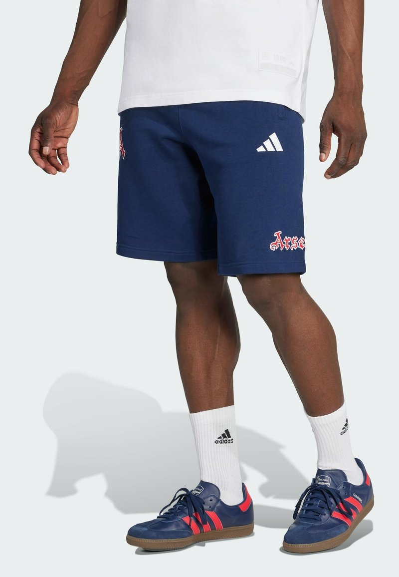 Marineblå atletisk shorts med rødt logo, lavet af bomuldsmateriale, lige ben design. Matchet med marineblå sko med røde striber og hvide sokker.