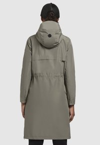 Parka lungă, de culoare verde măsline, cu talie strânsă, glugă și închideri cu capse. Textură netedă, siluetă dreaptă și detaliu cu buzunar pe spate.