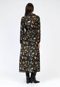 Robe longue noire à motifs, ornée de graphiques colorés tels que des animaux et des planètes, avec une taille cintrée et des manches longues. Portée avec des bottes noires à talons.