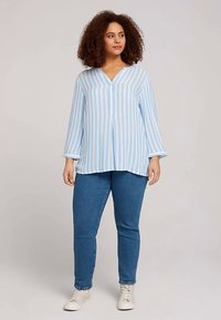 Hele sinine ja valge triibuline pluus V-kaelusega, pikkade varrukatega ja lõdva lõikega. Sobitatud siniste teksade ja valgete tossudega.