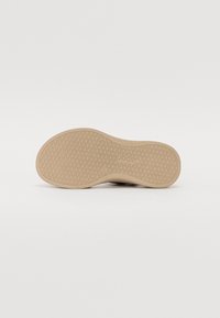 Shoe sole with a textured rubber surface, featuring a light beige color and a flexible shape, designed for traction and comfort.