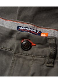 Pantaloni chino grigi con cuciture arancioni, dotati di un bottone nero e un'etichetta del marchio. Il tessuto sembra texturizzato e resistente. Taglia 30W.