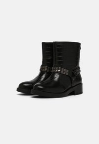 Bottines noires avec une texture en cuir de crocodile, un bandeau décoratif clouté au niveau de la cheville, et un petit talon carré pour plus de stabilité.