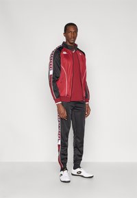 Dres z czerwonym żakietem z czarnymi akcentami, białym obramowaniem oraz dopasowanym czerwonym topem; czarne spodnie z czerwonymi paskami po bokach; białe trampki.