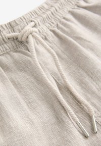 Primer plano de pantalones de tejido de punto beige con cinturilla elástica y cordón atado con extremos de metal.