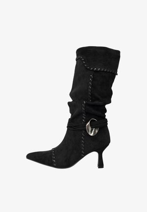 Bota de tobillo de ante negro con punta afilada, diseño fruncido, costuras decorativas, un acento de cuerda negra y un detalle circular plateado.