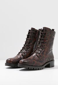 Stivaletti con lacci, in pelle sintetica con motivo in pitone marrone, texture lucida, suola robusta e sei coppie di occhielli per i lacci.