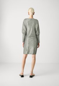 Rochie metalizată argintie, cu mâneci lungi, formă ajustată și textură moale. Prezintă un decolteu rotund și detalii la încheieturi. Purtați cu sandale cu curele.