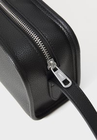 Borsa in pelle nera texturizzata con zip e accessori in argento. Presenta una forma rettangolare e una cinghia sottile per il trasporto.