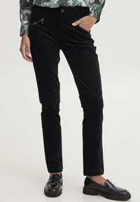 Black corduroy pants with a slim fit, featuring zippered pockets and subtle texture, paired with black loafers.