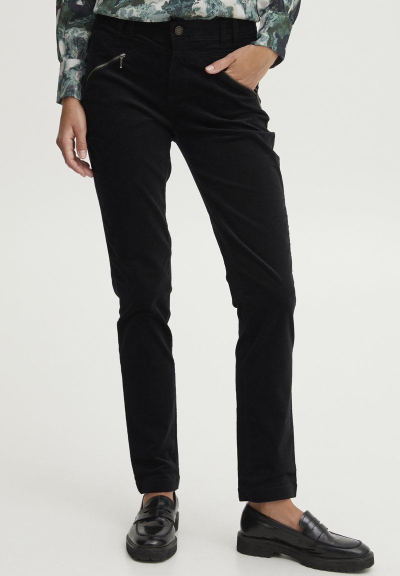Black corduroy pants with a slim fit, featuring zippered pockets and subtle texture, paired with black loafers.