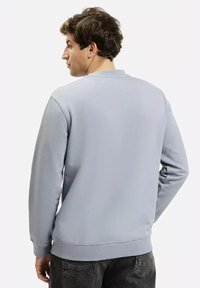 Jasnoszary sweter z okrągłym dekoltem, długimi rękawami i ściągaczami. Charakteryzuje się minimalistycznym wzornictwem oraz gładką, miękką fakturą.