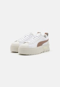 Weiße Plattform-Sneaker mit abgerundetem Zehenbereich, strukturierter beiger Sohle und braunem Akzentstreifen. Verfügt über ein Schnürdesign und eine Ziehschlaufe an der Ferse.