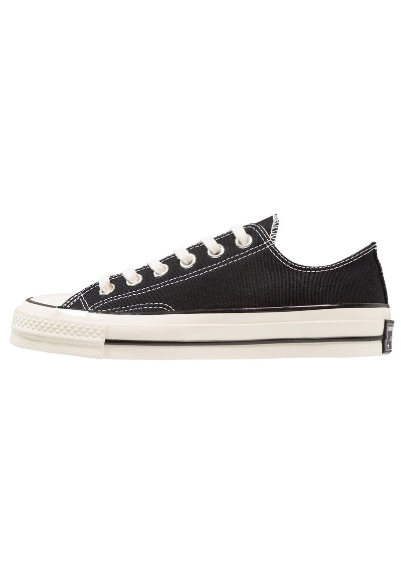 Sneaker basse en toile noire avec lacets blancs, semelle en caoutchouc blanche, et surpiqûres contrastantes, vue de profil extérieur sur fond blanc.