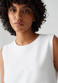 Weißes ärmelloses Top aus glattem Baumwollstoff, mit Rundhalsausschnitt und lockerer Passform, minimalistisches Design ohne Muster.