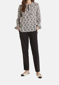 Blůza s černobílým vzorem, s volánkovými manžetami a výstřihem ve tvaru klíče, zkombinovaná s černými slim-fit kalhotami a dvoubarevnými balerínami.
