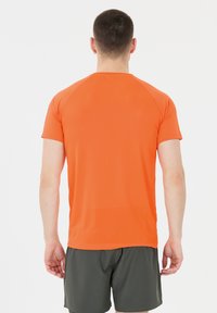 Oranssi lyhythihainen urheilupaita, jossa on rakennetta luova kuvio, pyöreä kaula-aukko ja raglan-hihat, yhdistetty tummaan harmaisiin shortseihin.