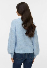 Gaiši zils, mīksti adīts džemperis ar balona piedurknēm, ribota apmale un brīvs piegriezums. Kombinēts ar tumši zilām džinsa biksēm.