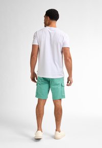Bílé tričko s krátkým rukávem v kombinaci s mentolově zelenými cargo šortkami. Obuv je světle zbarvená a dodává outfitu letní vzhled.