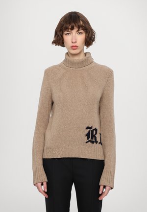 Beige gestrickter Rollkragenpullover mit gerippten Bündchen und Saum, der ein schwarzes stilisiertes Buchstaben-Design auf der unteren Vorderseite aufweist.
