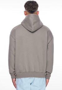 Grå hættetrøje med snor i hætten, løs pasform, ribbede manchetter og kant; båret med lyseblå jeans, der viser et blødt, tekstureret stof.