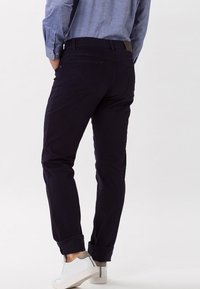 Pantalones de algodón azul marino con un corte ajustado, puños enrollados y bolsillos traseros. Combinados con zapatillas blancas y una camisa de botones azul claro.