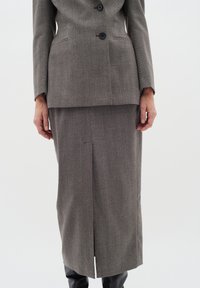 Sivý sako s herringbone vzorom na dva gombíky, skombinované s ladiacou sukňou s predným rozparkom, doplnené o čierne čižmy po kolená.