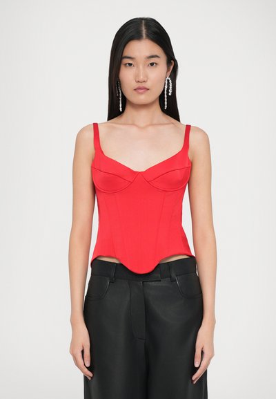 Top corset roșu, ajustat, cu cusături structurate, curele subțiri pe umeri și decolteu în formă de inimă. Asortat cu pantaloni de piele negri, cu talie înaltă.