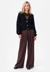 Czarny dziergany kardigan z dekoltem w serek, trzema dużymi guzikami i teksturowanym wzorem, w połączeniu z szerokimi spodniami w brązowe prążki.