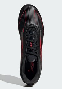 Chaussure de sport noire avec texture nervurée, accents rouges et design à lacets. Présente un profil élégant et un intérieur noir lisse.