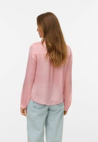 Blouse rose clair en tissu transparent, dotée de manches longues, de poignets à boutons et d'un ourlet arrondi. Design simple avec des accents minimalistes.
