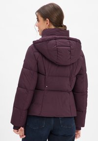 Korte, paarse pufferjack met capuchon, voorzien van een gewatteerde textuur en geribde manchetten. Het ontwerp heeft een cropped snit en minimale hardwaredetails.