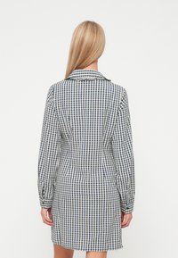Φόρεμα πουκαμίσα σε καρό navy και άσπρο, με μακριά μανίκια, αιχμηρό γιακά και κουμπωτές μανσέτες. Λείος ύφασμα με κομψή εφαρμογή.
