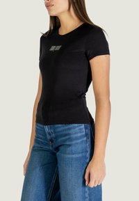 Maglietta nera in cotone con maniche corte, scollo rotondo e scritta bianca sul davanti, abbinata a jeans di denim blu.