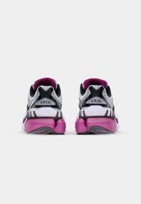 White and black athletic shoes with a textured mesh upper, pink accents on the sole, and a curved design at the heel.