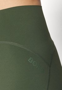 Žalios sportinės legging kelnės su lygiu paviršiumi, su siuvinės siūlės ir subtiliu „BORG“ prekės ženklo žymėjimu, suderintu žalios spalvos.