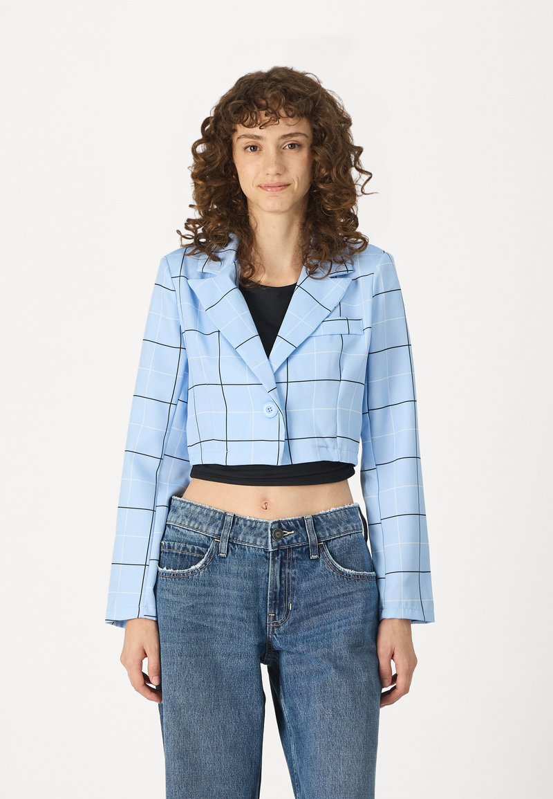 Kuttet blå blazer med hvitt rutenett mønster, lange ermer, notched krage, enkel knappelukking, brukt over en svart topp og paret med blå jeans.