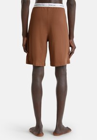 Bruine katoenen shorts met een elastische tailleband en een witte logoband. De shorts hebben een ontspannen pasvorm en een lengte tot halverwege de bovenbenen.