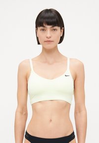 Soutien-gorge de sport jaune clair avec un design en V, des bretelles fines et un petit logo noir sur le côté gauche. Texture lisse, style minimaliste.