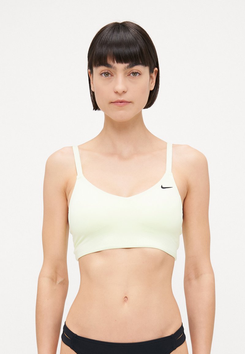 Soutien-gorge de sport jaune clair avec un design en V, des bretelles fines et un petit logo noir sur le côté gauche. Texture lisse, style minimaliste.