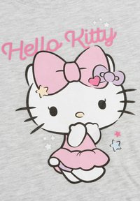 T-shirt grigia con una grande grafica di Hello Kitty che indossa un fiocco e un vestito rosa, impreziosita da piccole stelle colorate e dalla scritta "Hello Kitty" in rosa.