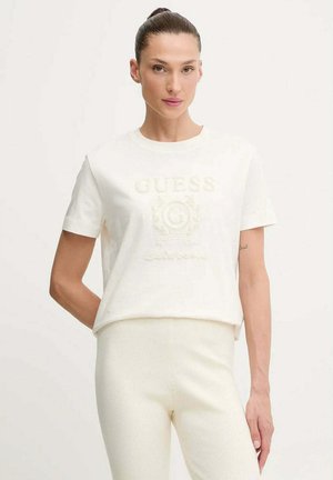 Maglietta in cotone bianco con logo "GUESS" in rilievo, scollo rotondo e maniche corte, abbinata a pantaloni color crema a coste.