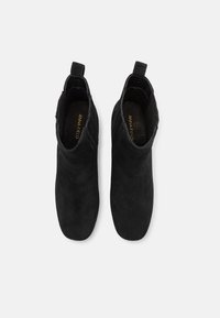 Botas de tobillo de ante negro con una textura suave, que presentan una pestaña de bucle en la parte posterior y un diseño de punta almendrada.