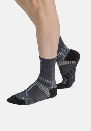 Legs wearing dark gray and black athletic ankle socks with light gray patterns, one foot flat and the other raised on toes.