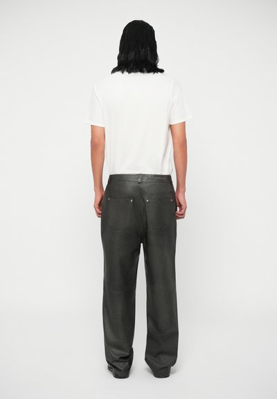 Pantalones de cuero negro con un ajuste ligeramente holgado, con un acabado texturizado y diseño de cinco bolsillos. Llevados con una camiseta de algodón blanca.