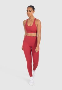 Red sports bra and high-waisted leggings made of stretchy fabric. The matching set features subtle branding and a smooth texture, paired with white sneakers.