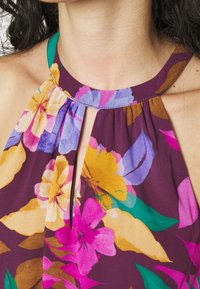 Close-up of a neckline showing a sleeveless floral dress with purple, yellow, pink, and green patterns and a keyhole cutout detail.