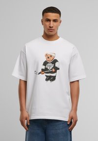 White oversized t-shirt with short sleeves featuring a graphic of a bear in a hockey uniform holding a hockey stick. Casual fit.